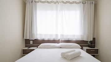 A hotel room with a large bed, two bedside tables, a remote control, and a rolled towel on the bed.
