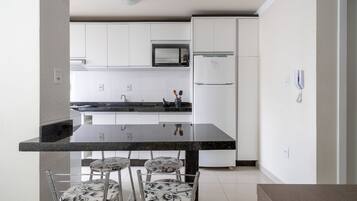 Cozinha moderna com armários brancos, bancada preta e área de refeições com quatro cadeiras.