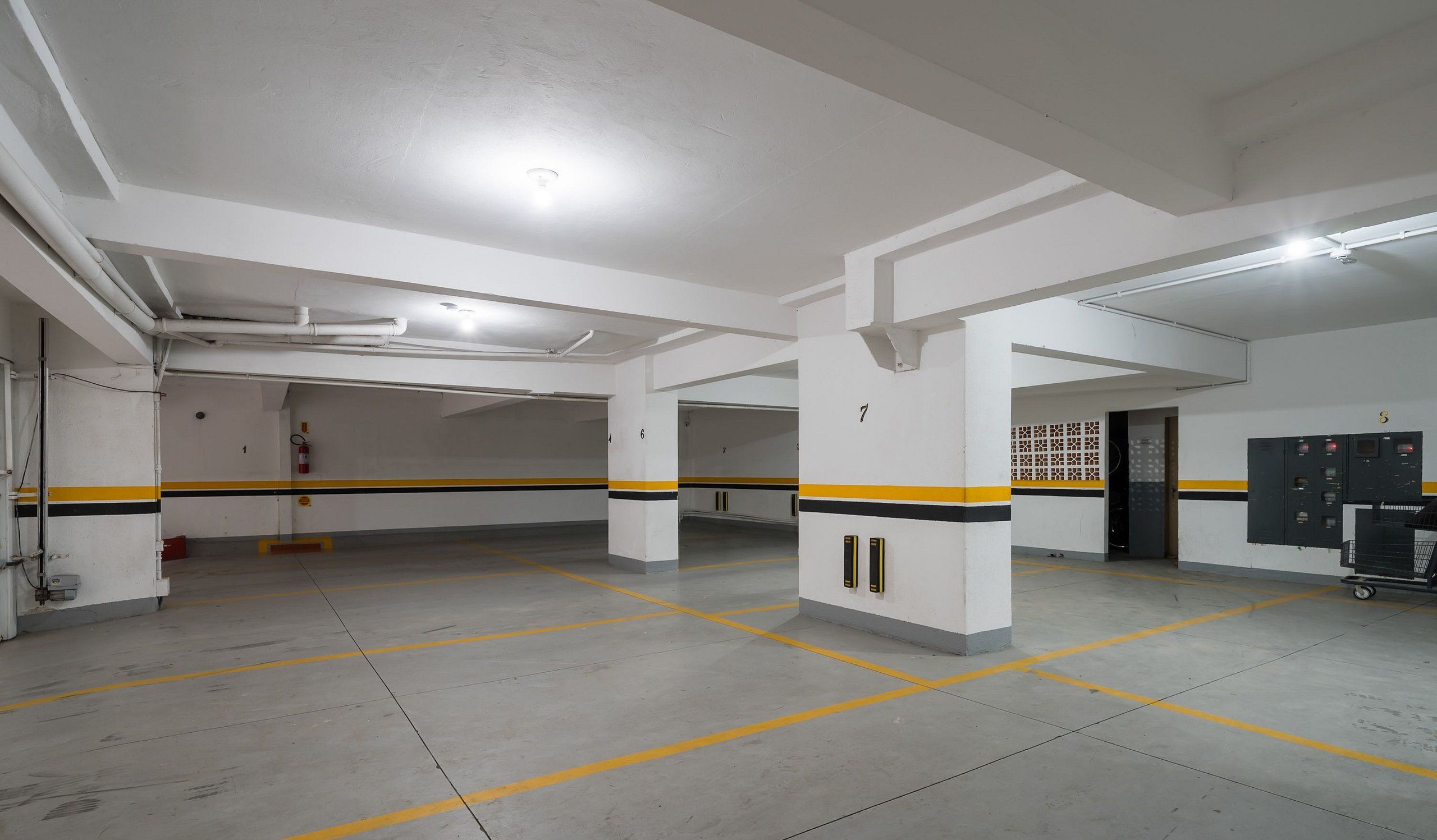 Uma garagem de estacionamento com paredes brancas, faixas amarelas e pretas e vagas numeradas.