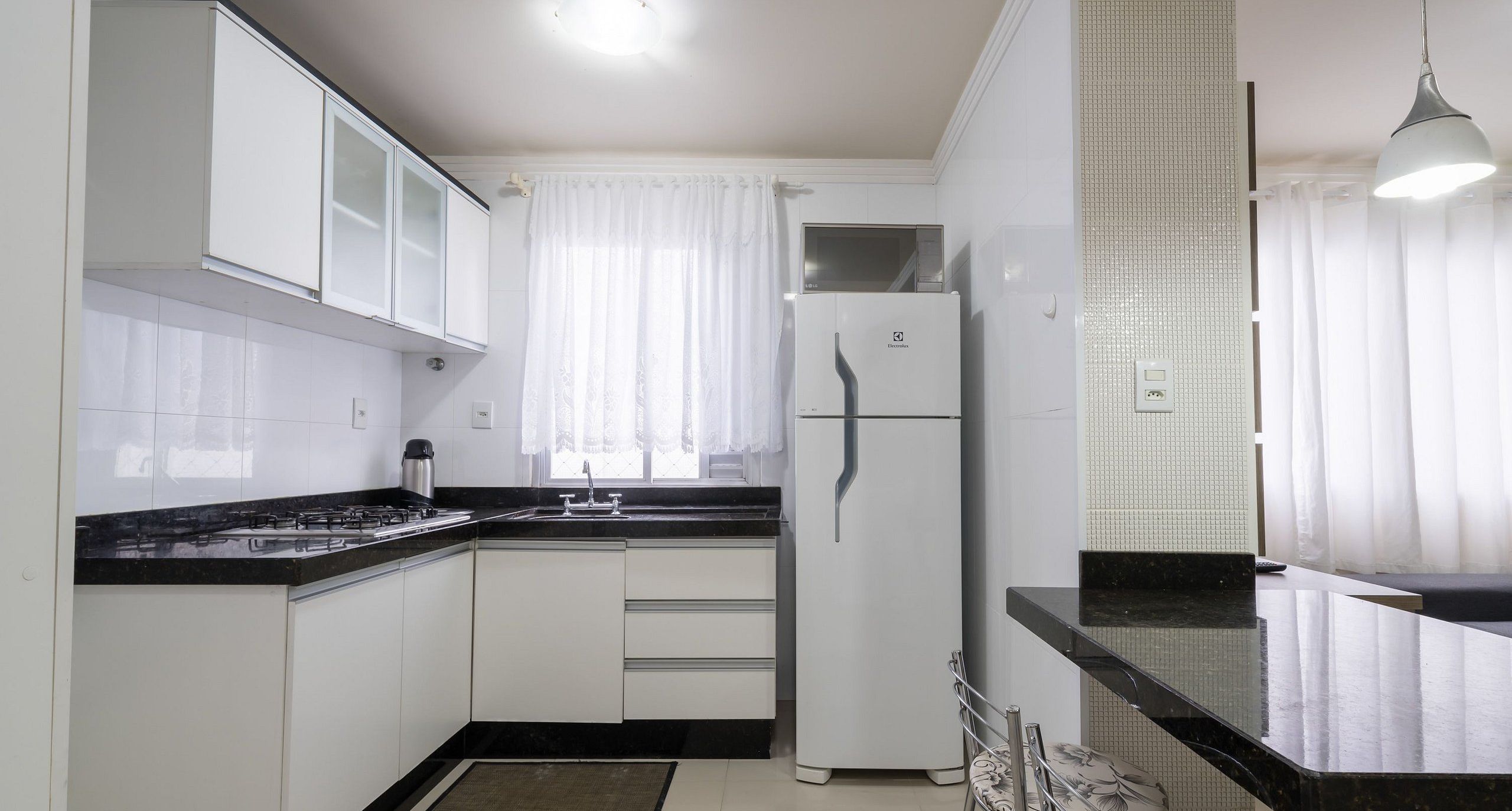 A kitchen with white cabinets, a black countertop, a stainless steel sink, and a white refrigerator.