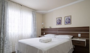Habitació d'hotel amb un llit gran, dues taules de nit, un capçal de llit i dos quadres florals emmarcades a la paret.