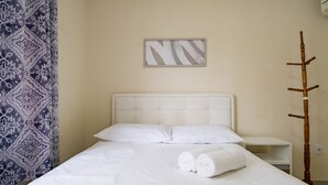 Una cama bien hecha con sábanas blancas, una cortina estampada, una obra de arte colgada en la pared y un perchero de madera.