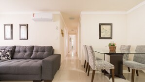 Una sala de estar moderna con un sofá gris, una mesa de comedor con sillas y un pasillo que conduce a otra habitación.