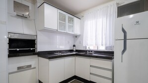 Una cocina con gabinetes blancos, una encimera negra, una campana extractora de acero inoxidable y un refrigerador.