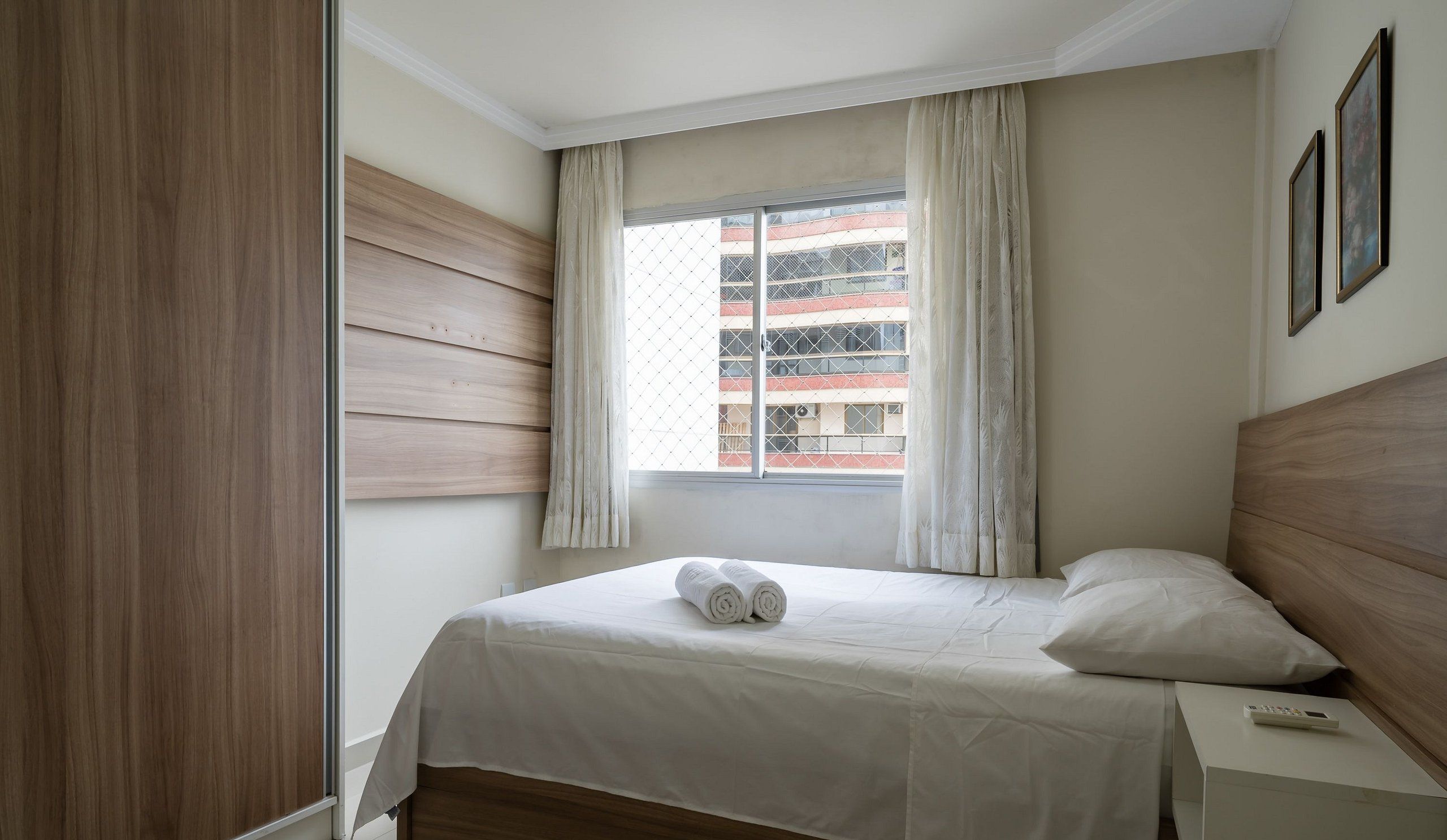Une chambre d’hôtel avec un lit, une table de chevet, une fenêtre avec des rideaux et une vue sur les bâtiments environnants.