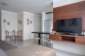 Quarto de hotel moderno com uma cama, televisão, área de refeições com cadeiras e cozinha equipada com frigorífico.