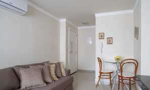 Een woonkamer met een bank, een eettafel met stoelen en een kleine keukenhoek.