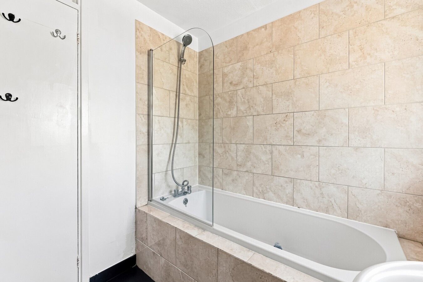 A bathroom with a bathtub, a shower, and beige tiled walls.