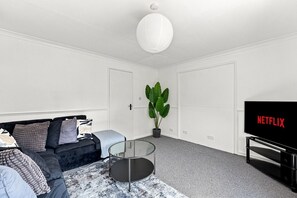 Ein modernes Wohnzimmer mit einer Couch, einem Glastisch, einem Blumentopf und einem Fernseher mit dem Netflix-Logo.