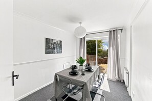 A dining area with a table set for four, a potted plant, and a cityscape photograph on the wall. - Arbour House • Sleeps 5 • Free Parking • Spacious Garden • Fast Wifi • Self-Check-In • Yoko Property (Northampton)