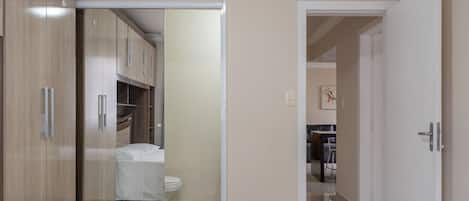 Quarto de hotel com cama, um guarda-roupa e um banheiro visível por uma porta aberta.