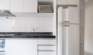 Cocina con gabinetes blancos, encimera negra, microondas, refrigerador y estufa.