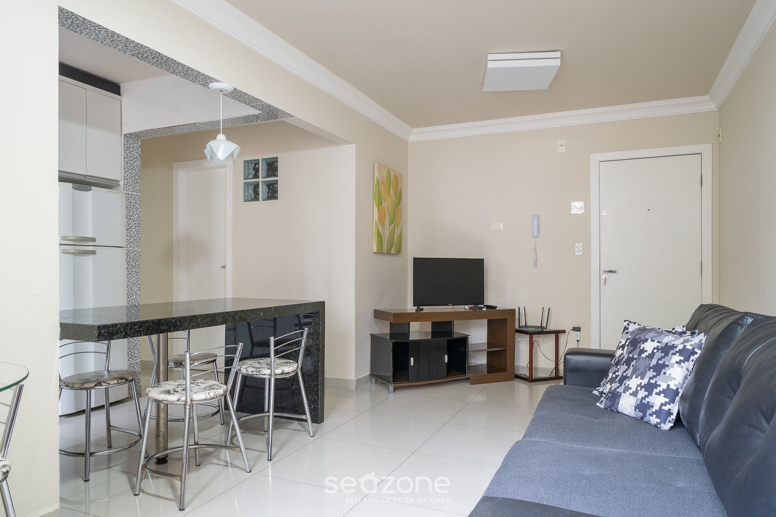 A modern living room with a sofa, a dining area with chairs, a TV, and a kitchen area.