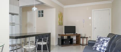 Una sala de estar moderna con un sofá, un comedor con sillas, un televisor y una zona de cocina.