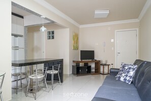 Una sala de estar moderna con un sofá, un comedor con sillas, un televisor y una zona de cocina.