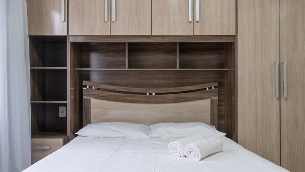 A bed with white linens and two rolled towels, a wooden headboard, and a built-in wardrobe with multiple compartments. - Apt 140m From Beach Close to Attractions BC Eac404 (Balneário Camboriú)