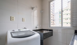 Ein Badezimmer mit Waschmaschine, Waschbecken und einem Fenster mit Blick auf Gebäude.