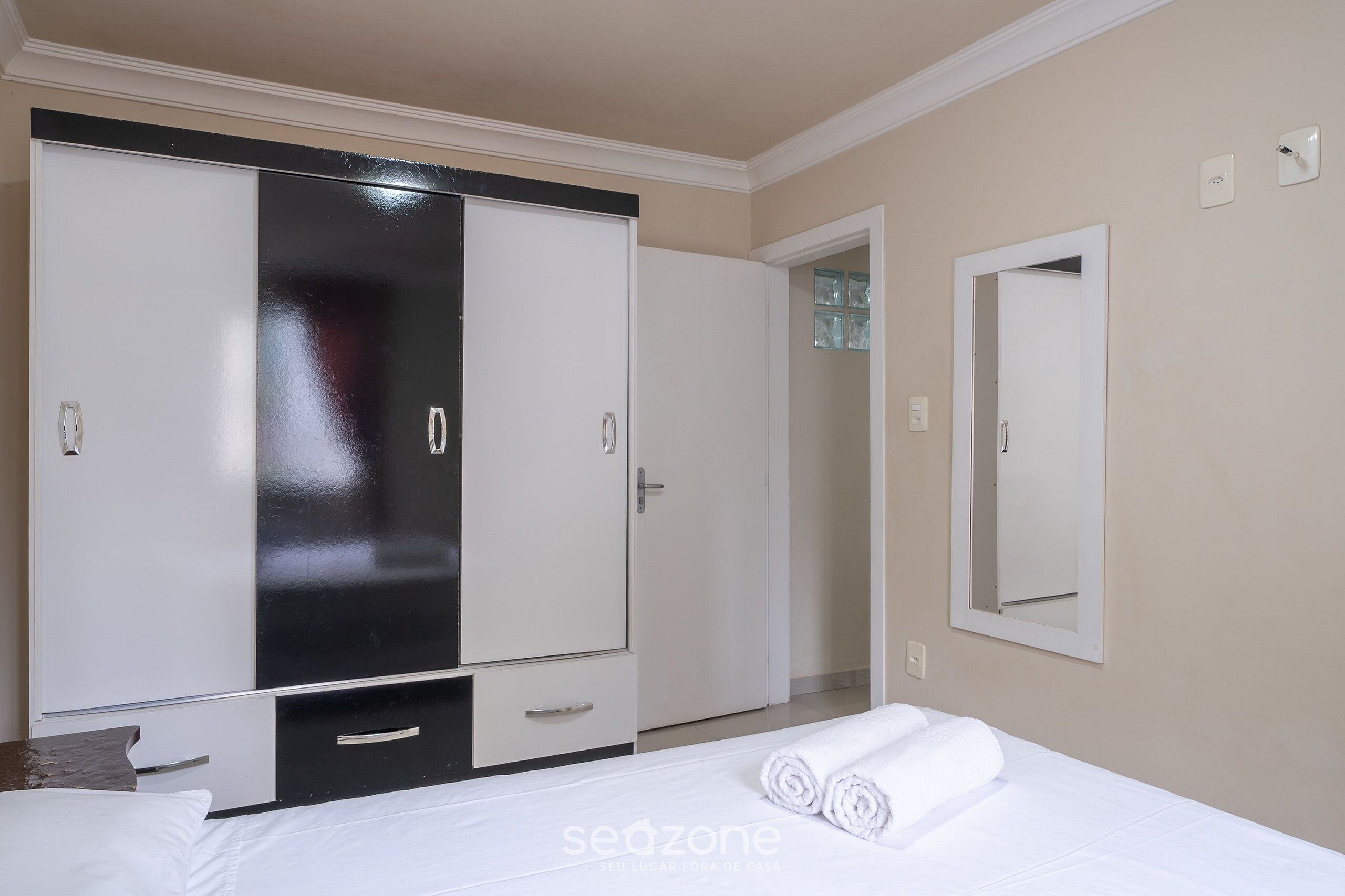 Un dormitorio con una cama, un armario amplio, un espejo y una puerta que da a otra habitación.