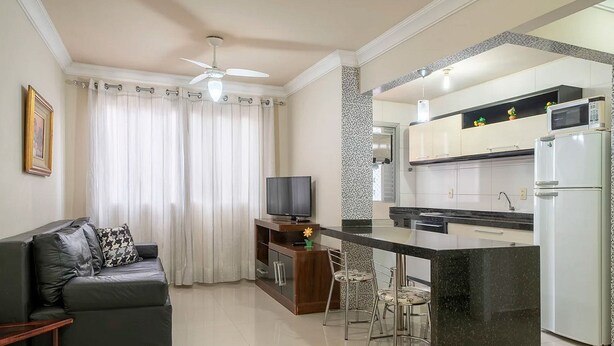 Una cocina moderna con una isla central, una zona de comedor con taburetes de bar, un sofá con televisor y un ventilador de techo.