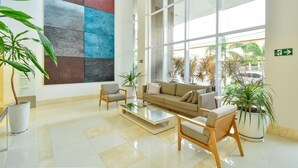 A spacious lobby with a large abstract art piece, comfortable seating, and large windows offering a view of the outdoors. - Flat w/ Pool in Setor Bueno - Dnag1701 (Goiânia)