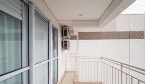 Un balcón con barandal blanco, puerta de vidrio y pared de azulejos con un diseño geométrico.