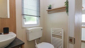 Um banheiro pequeno com vaso sanitário, pia, janela com persianas, radiador e prateleira com uma planta.