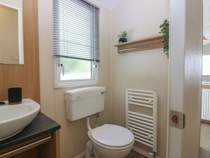 Ein kleines Badezimmer mit Toilette, Waschbecken, einem Fenster mit Jalousien, einem Heizkörper und einem Regal mit einer Pflanze.