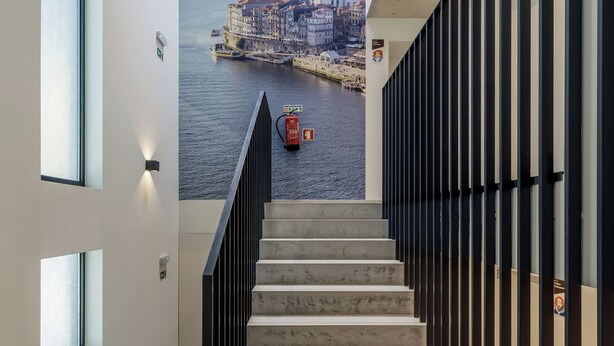 A staircase with a cityscape mural at the top, a fire extinguisher, and a fire hose on the landing. - Marina da Afurada Apartments - Fernando Pessoa (Vila Nova de Gaia)