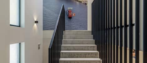 A staircase with a cityscape mural at the top, a fire extinguisher, and a fire hose on the landing.