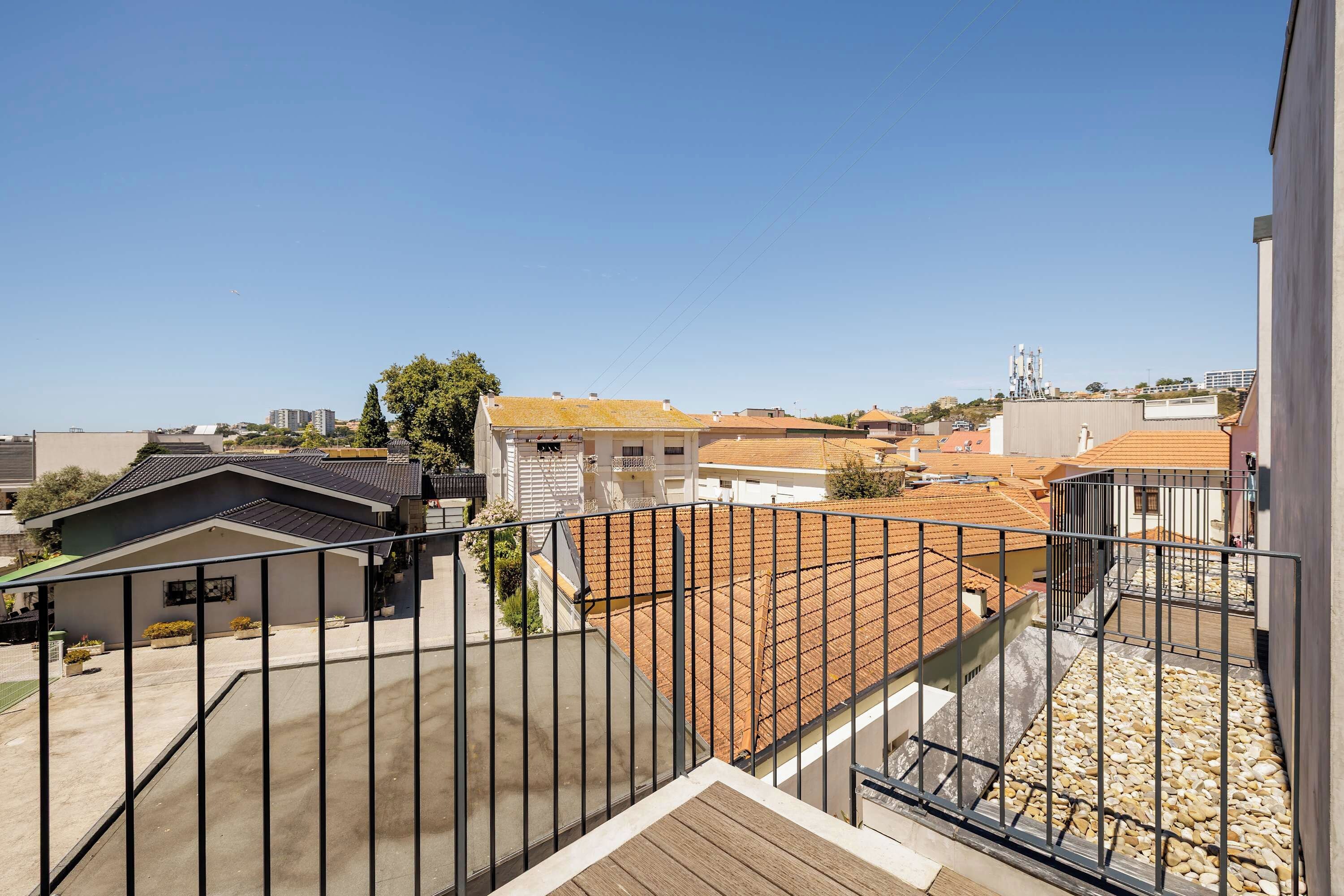 Un quartier résidentiel offrant une vue sur un immeuble doté d’un toit en tuiles, d’un balcon avec une rambarde en métal et d’un ciel bleu dégagé.