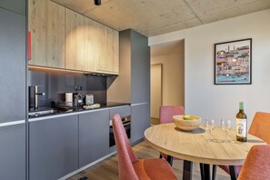 Eine moderne Küche mit grauen Schränken, einer Holzausziehtafel und einem Essbereich mit rundem Tisch und orangefarbenen Stühlen.