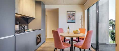A modern kitchen with grey cabinets, a built-in oven, and a dining area with a round table and orange chairs.