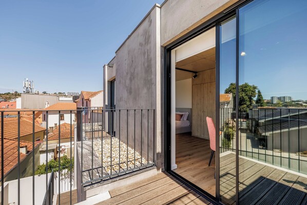 Un appartement moderne doté d’un balcon, de planchers en bois et d’une grande porte vitrée donnant sur une chambre.