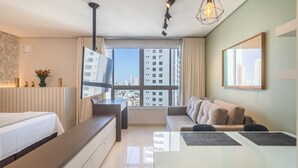 Een moderne hotelkamer met een bed, een bank, een eettafel en een groot raam met uitzicht op de stad.