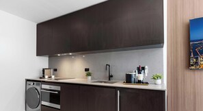 A modern kitchen with dark cabinetry, stainless steel appliances, and a cityscape painting on the wall. - Design Studio - Miami Pulse E11EVEN (Miami)