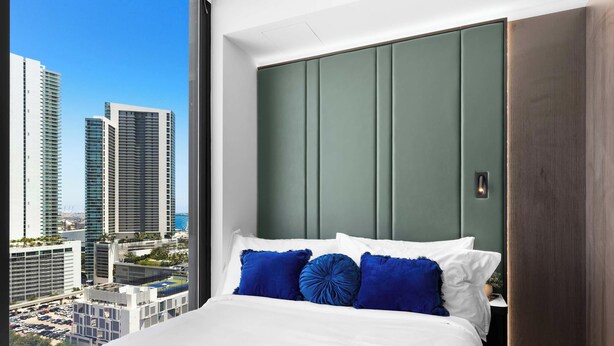 A modern hotel room with a large bed, a city view, and a green accent wall. - Design Studio - Miami Pulse E11EVEN (Miami)