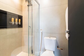 Ein modernes Badezimmer mit einer gläsernen Duschkabine, einer Toilette und einem schwarzen Ablageschrank mit Pflegeprodukten.