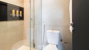 Ein modernes Badezimmer mit einer gläsernen Duschkabine, einer Toilette und einem schwarzen Ablageschrank mit Pflegeprodukten.