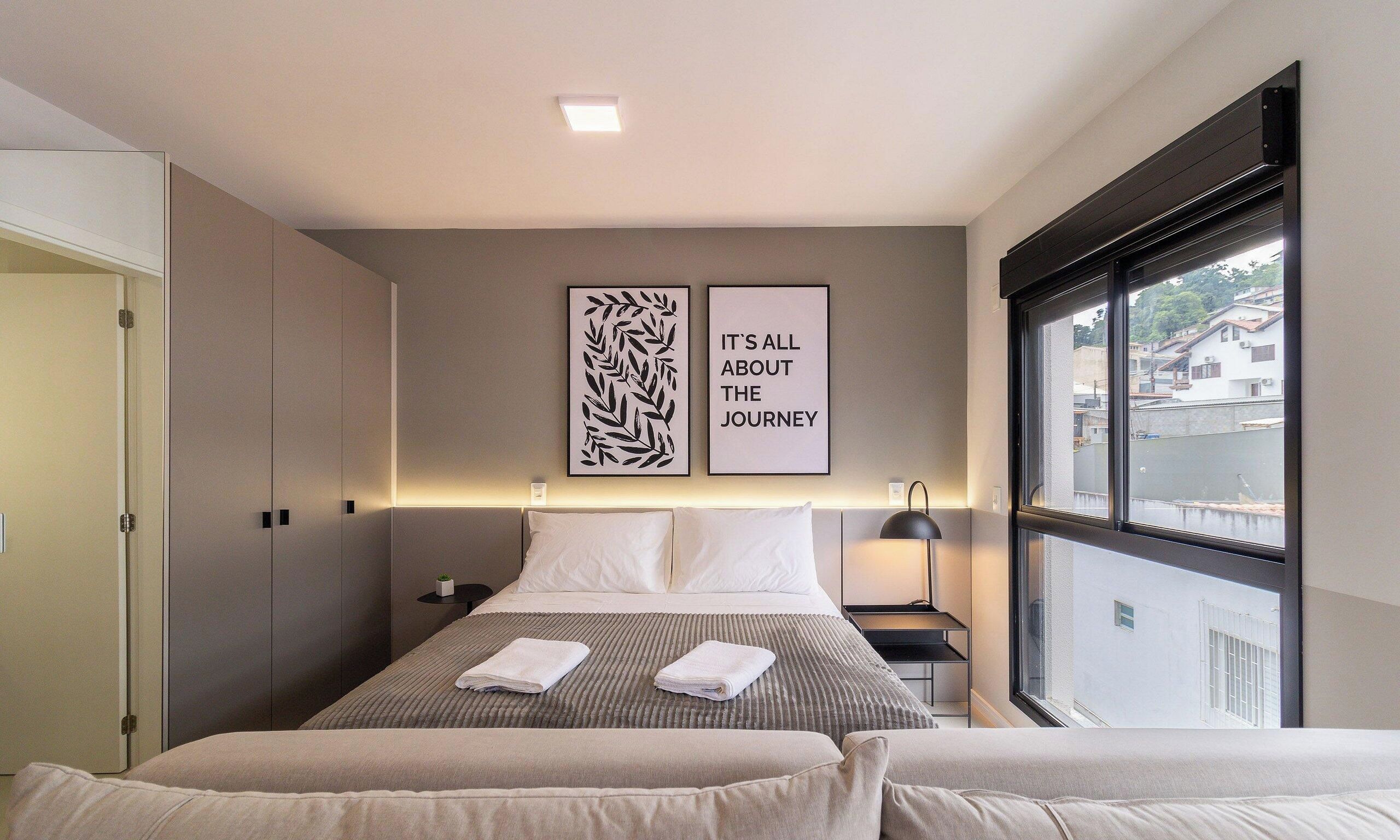 Una habitación de hotel con cama, dos mesitas de noche, ventana con vistas y dos obras de arte en la pared.