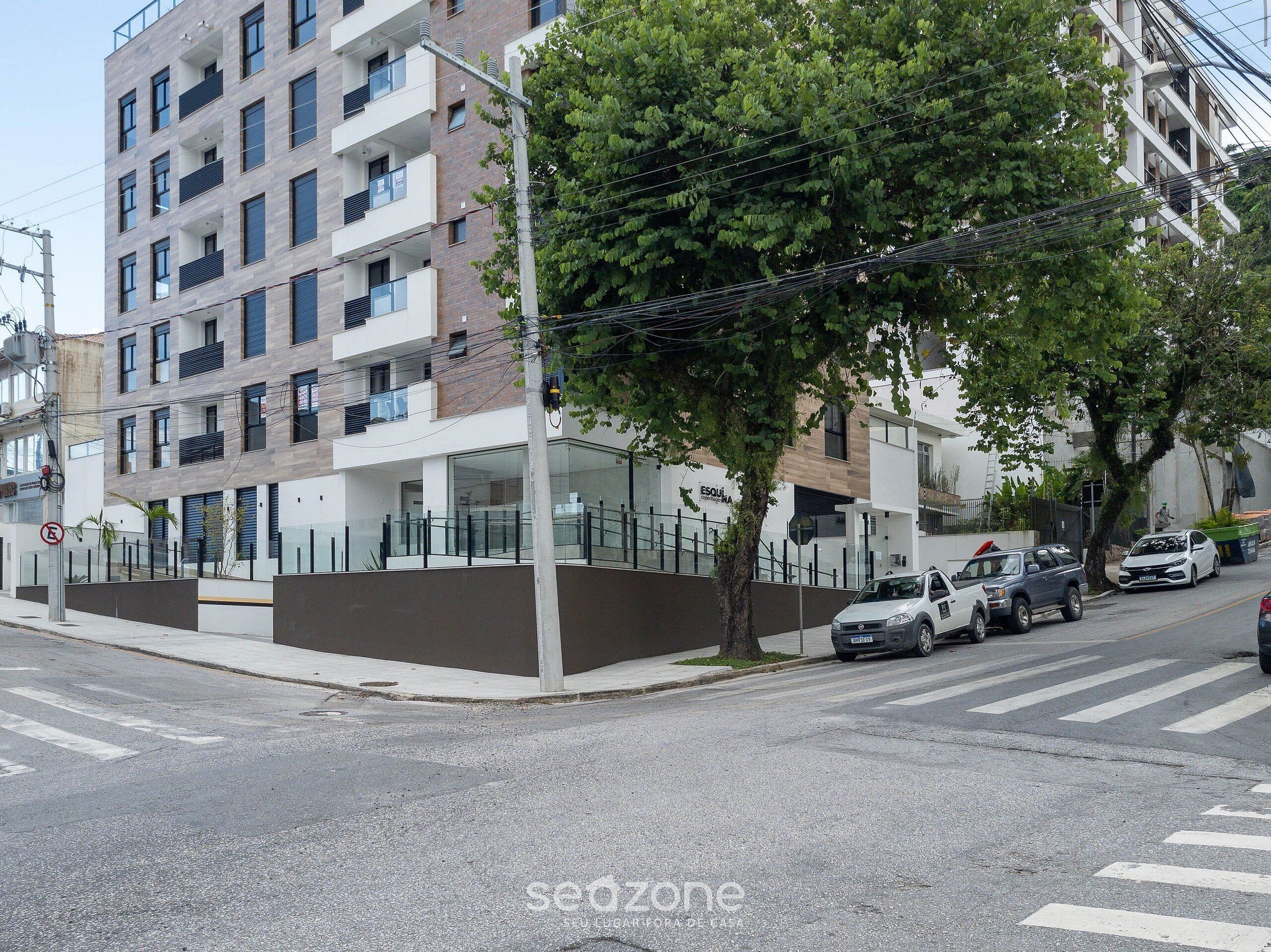 A multi-story residential building with balconies, a gated entrance, and parked cars on the street.