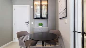 Un área de comedor moderna con una mesa redonda y cuatro sillas, un mueble bar con puertas de vidrio y un cuadro abstracto enmarcado en la pared.