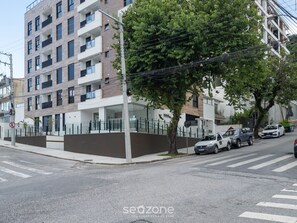 Un edificio residencial de varios pisos con balcones, entrada protegida por una reja y automóviles estacionados en la calle.