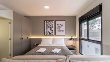 Una habitación de hotel con una cama, dos mesitas de noche, una ventana y dos obras de arte en las paredes.