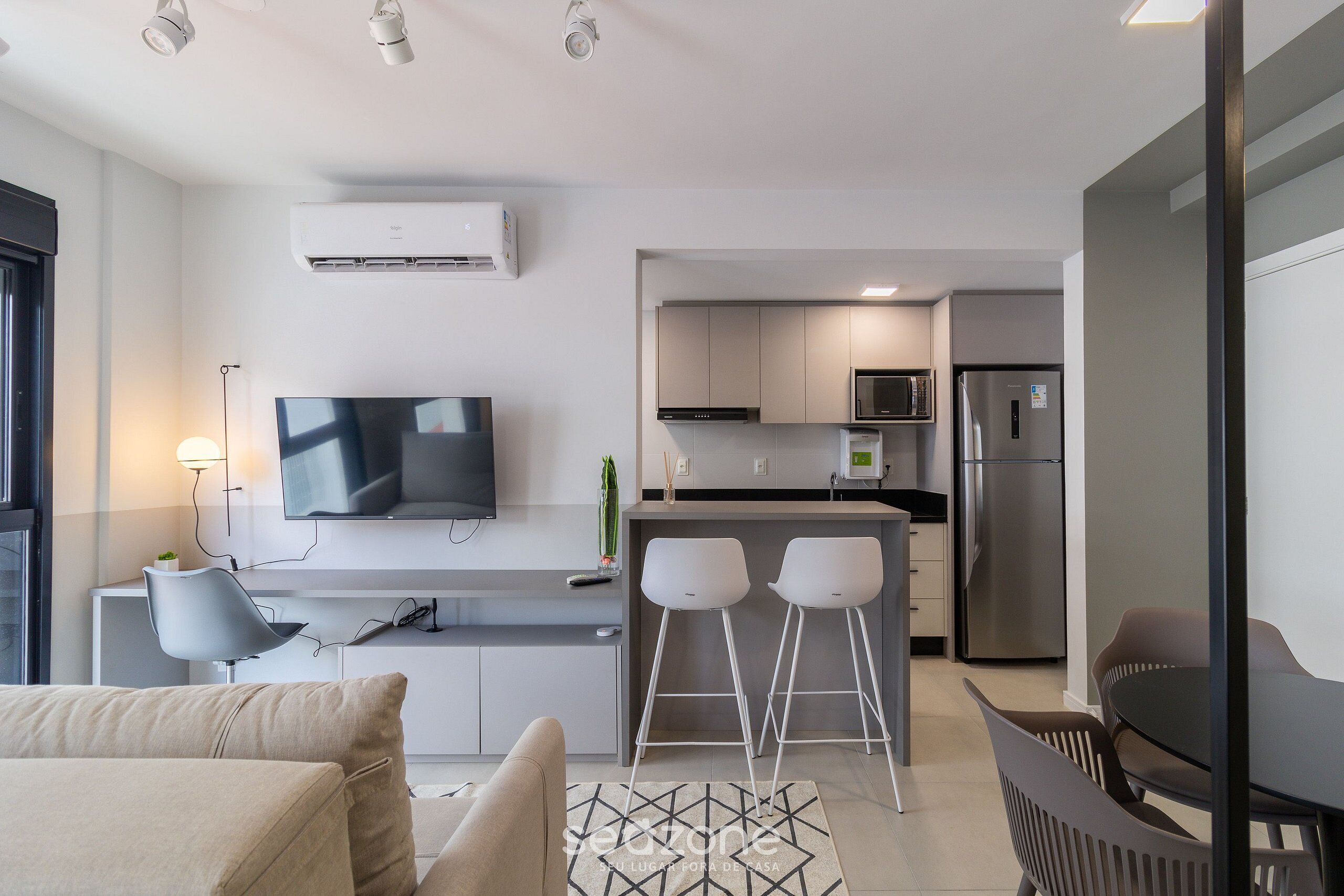 Una cocina moderna con un televisor de pantalla plana, dos taburetes de bar y un refrigerador.