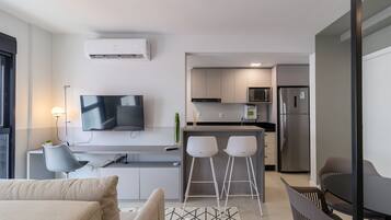 Una cocina moderna con un televisor de pantalla plana, dos taburetes de bar y un refrigerador.