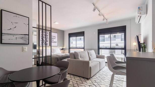 A modern hotel room with a sofa, a dining table, and chairs. There are large windows and artwork on the walls. - Apt in the Center Close to Beach in Floripa Ech113 (Florianópolis)