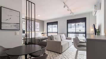 Habitación de hotel moderna con sofá, mesa de comedor y sillas. Cuenta con ventanas amplias y obras de arte en las paredes.