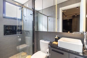 Ein modernes Badezimmer mit einer gläsernen Duschkabine, einer weißen Toilette und einem großen Spiegel über dem Waschbecken.