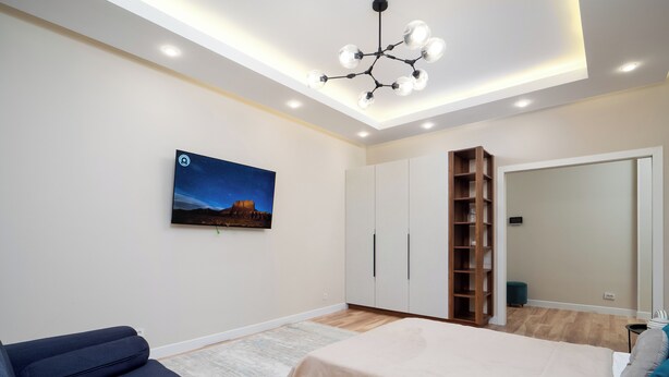 A modern bedroom with a bed, a sofa, a nightstand, a wardrobe, and a ceiling light fixture. - Comfort 1-room apartments  (Almaty)