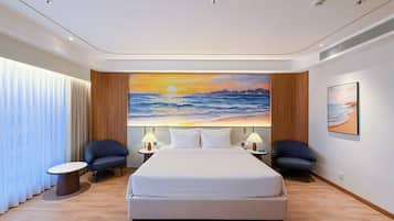 A hotel room with a large bed, two bedside tables, a nightstand, a chair, and a painting of a sunset over the ocean.